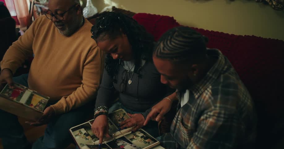 A family sits closely together on a couch looking at photo albums or books in a warmly lit room