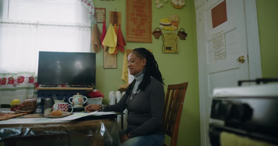 A woman is sitting at a dining table in a cozy kitchen working on paperwork or taxes
