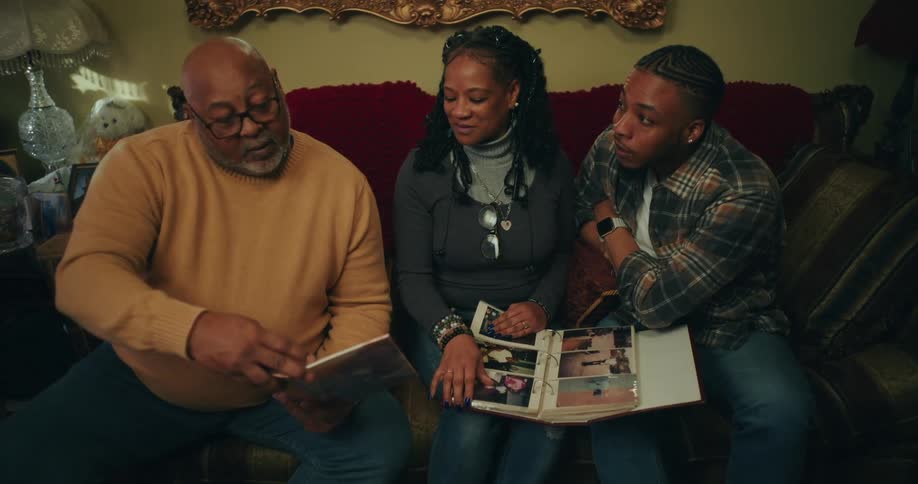 A family sits closely together on a couch looking at photo albums or books in a warmly lit room