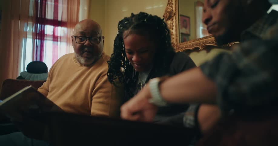 A family sits closely together on a couch looking at photo albums or books in a warmly lit room