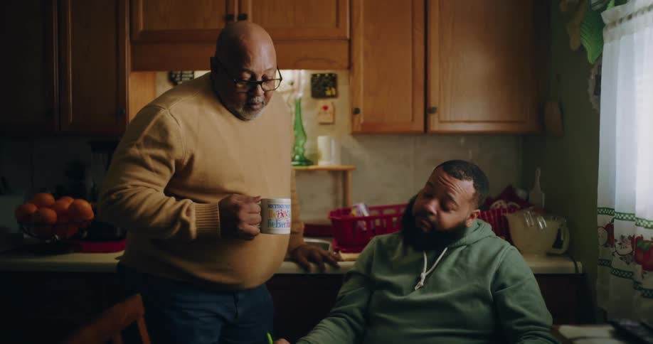 Two men with one of them holding a mug talking to the other in the kitchen