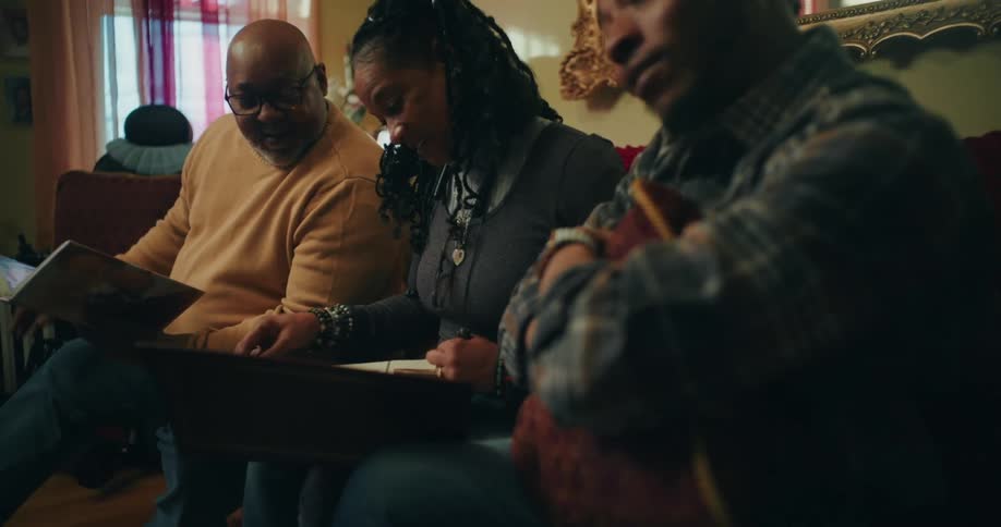 A family sit are sitting on a couch looking through a photo album