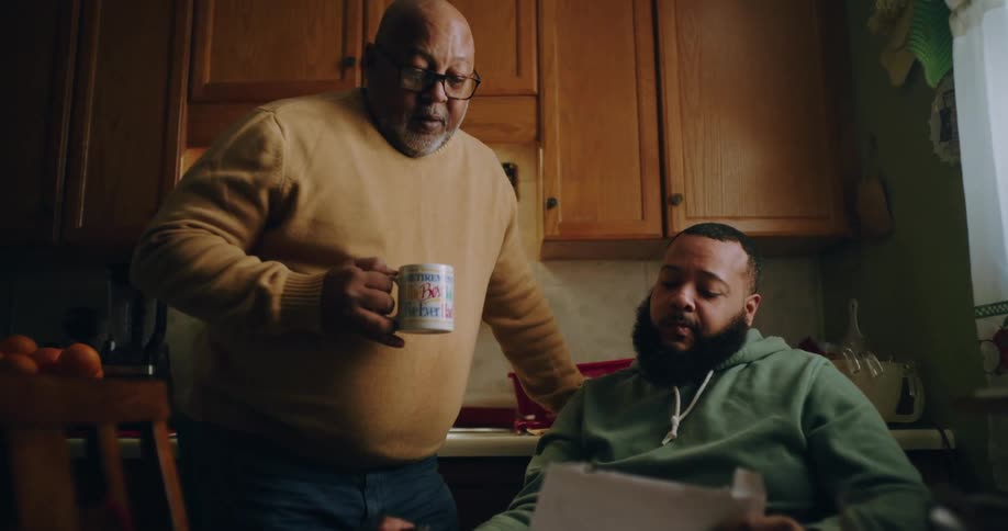 Two men in the kitchen with one of them standing talking to each other