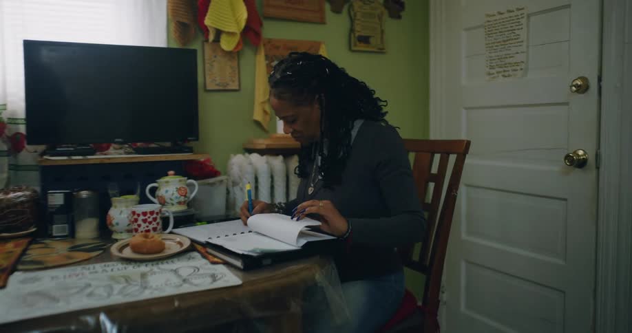 Woman frowns and makes a note while sitting at a table in the kitchen