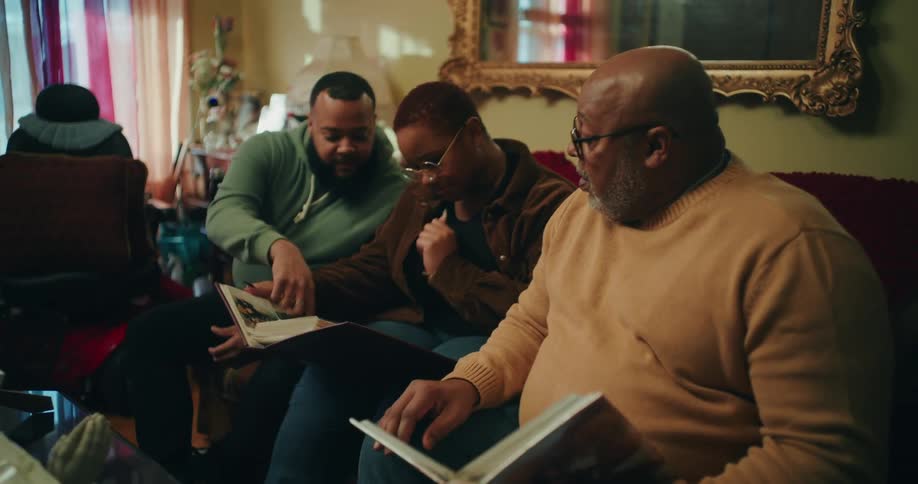 Three people sitting in an armchair in the living room and looking at photo albums