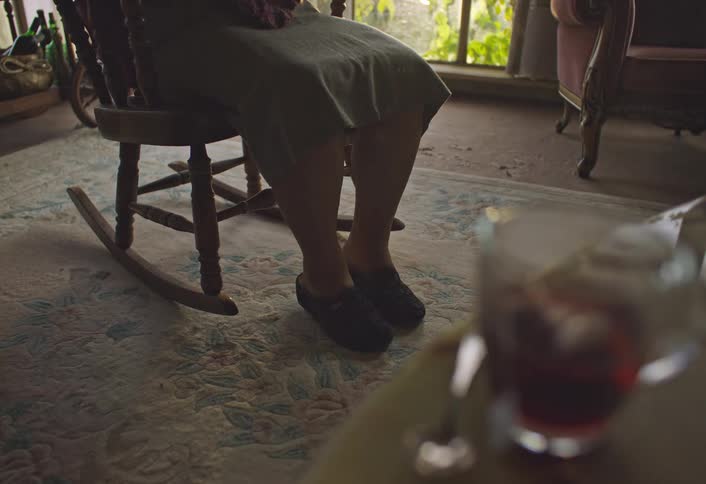 A woman is sitting in a rocking chair with tea on a table nearby