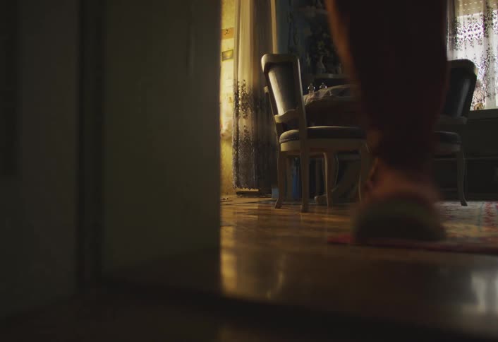 A person holding a backpack there in his hand is running in a living room and bumping into a chair
