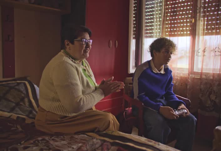 An older woman smiles and applauds a young man playing a video game