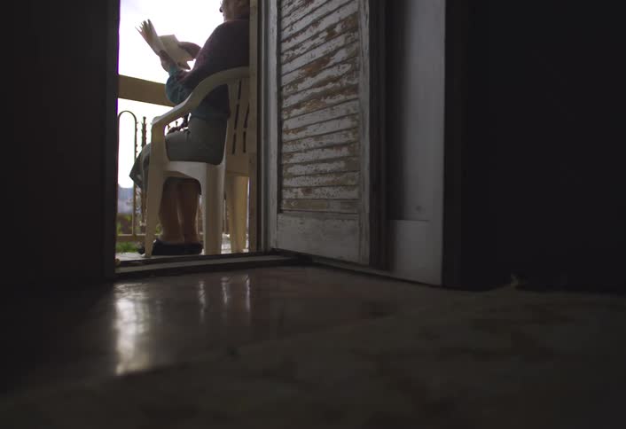 Older woman sits on a chair on the balcony to read during the daytime