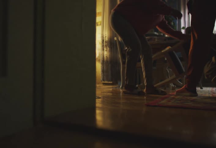 A person running into a room and knocking over a chair then another person picks it up