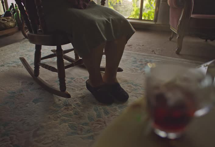 Woman rocks in a rocking chair while steam rises from a cup of tea nearby