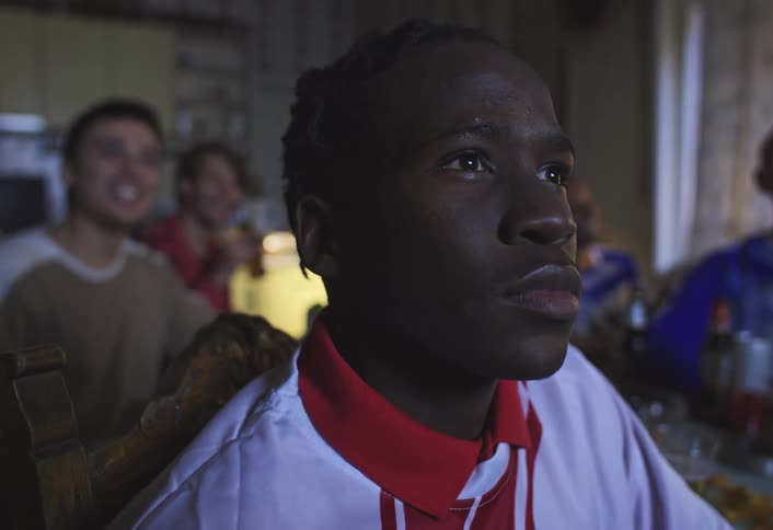 Portrait of a young man looking forward while sitting at a table with other friends