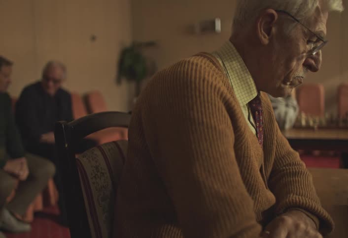 Side portrait of an elderly man sitting at a table concentrating
