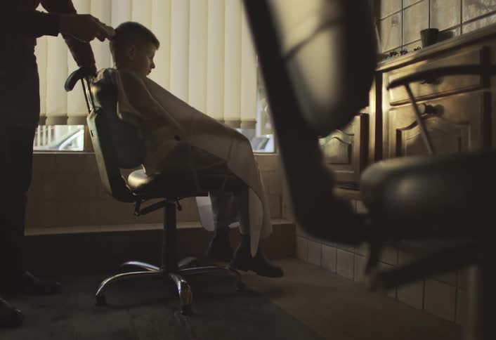 A barber is cutting a childs hair in a vintagestyle barbershop with wooden furniture