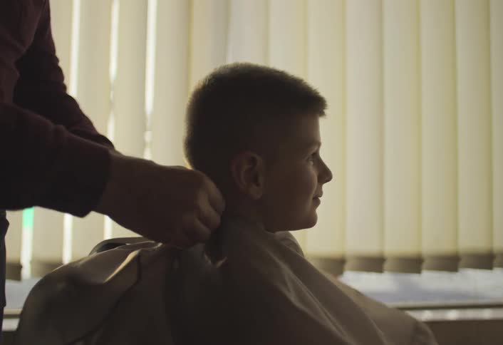 Pair of hands of a barber putting on an apron to cut a boys hair