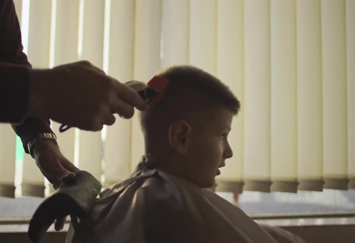 A barber is using a razor on a boys hair