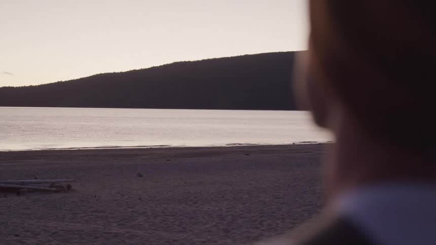 Man watches the sea at sunset with a mountain and lake in the background