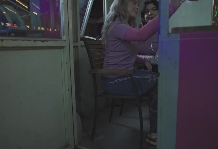 Two women sitting inside a booth take a selfie at a litup amusement park