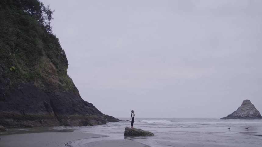 Woman with arms outstretched and looking up while standing on a rock by the sea