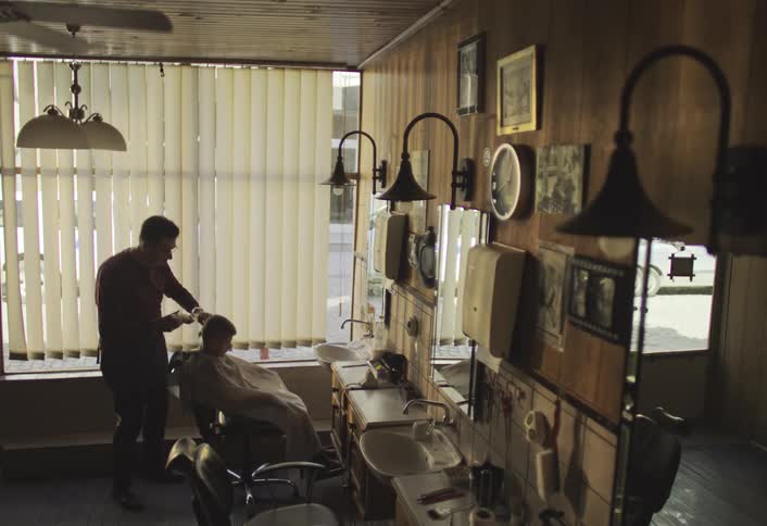A barber is cutting a childs hair in a vintagestyle barbershop with wooden walls mirrors and various framed pictures and decorations