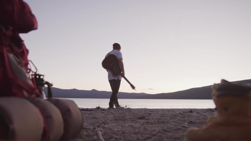 A man walks by the lake with his guitar