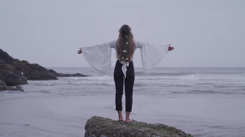 A woman is on the beach standing on a rock