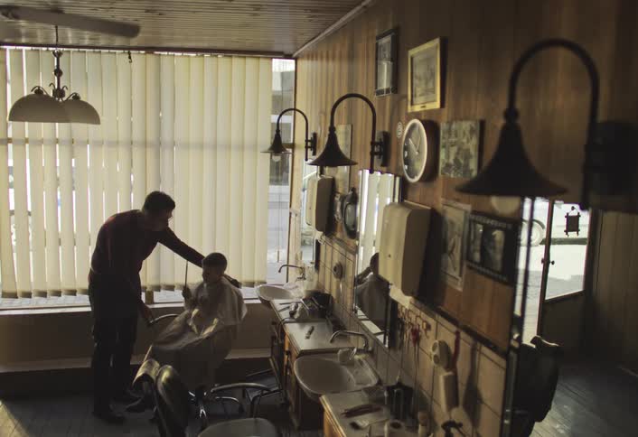 Barber turning the chair in which a boy is sitting holding a mirror and observing his haircut