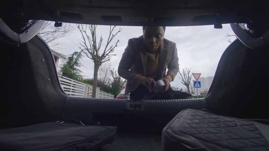 A man removes a plastic sheet and duct tape from his trunk