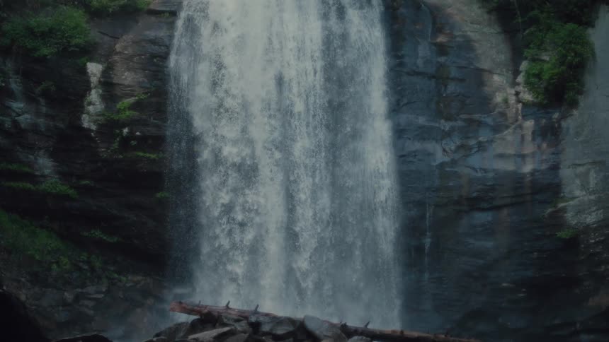 Looking glass falls plunges powerfully over a rocky cliff in a lush forest setting illuminated by sunlight filtering through the trees