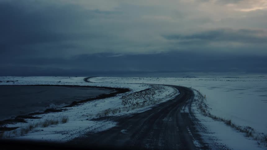 An elevated road curves through snow covered flat land just after sunset