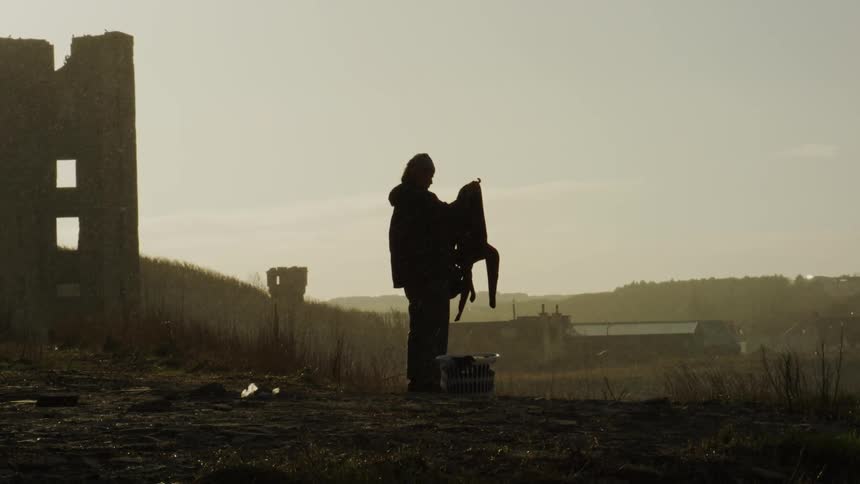Silhouette of a person handling a jacket in a field