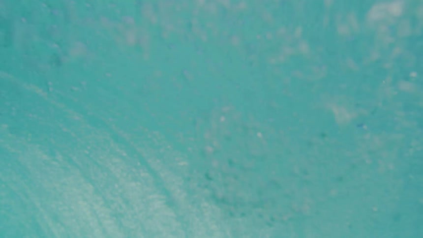 Sunlight filters through swirling ocean waves creating a textured bluegreen abstract pattern