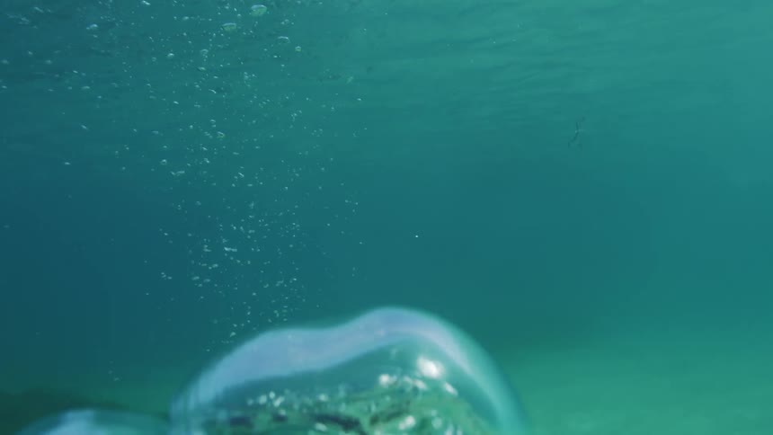 Scuba diver floating near the seafloor releases a large bubble that breaks into smaller bubbles while rising towards the surface