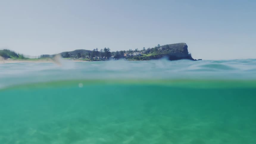 Blue waves flow over the seafloor in the the shallow waters near a coastal town on a sunny day