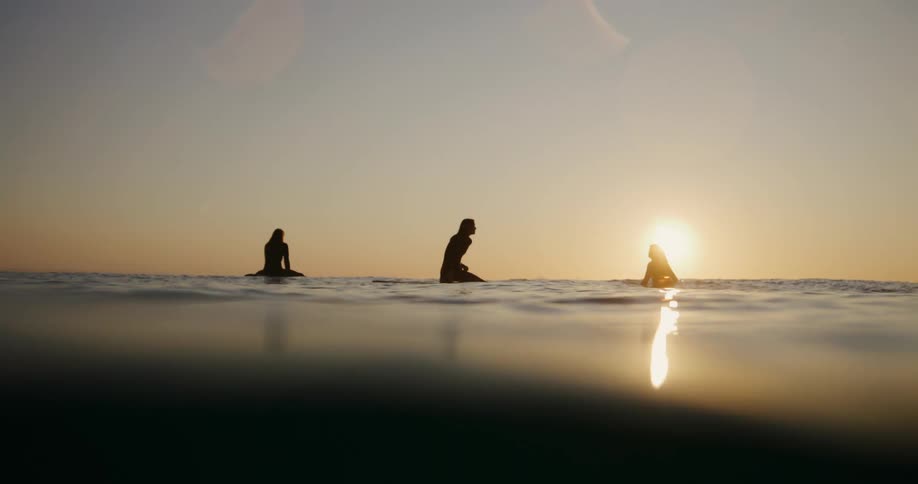 People are sitting on their surfboards in the water watching the sunrise