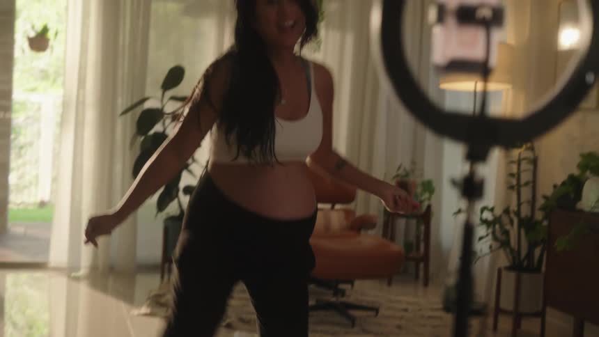 Pregnant woman dances and smiles in front of a ring light with a cell phone