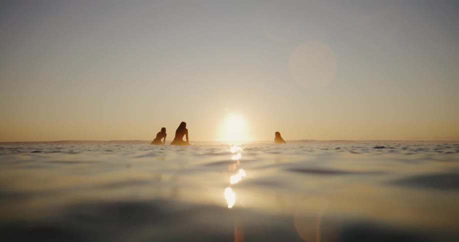 Three surfers are sitting on surfboards in the ocean at sunset