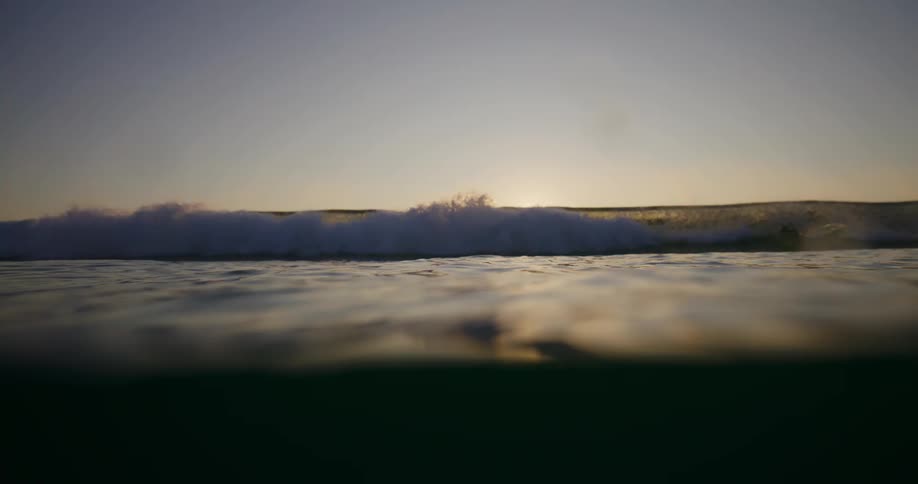 Interior view from inside the ocean with the sun on the horizon and the silhouette of some people