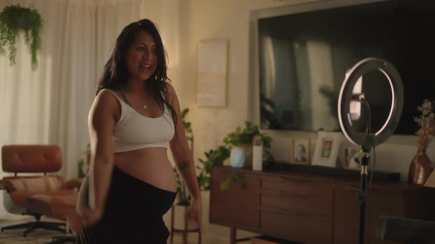Pregnant woman smiles while dancing in front of a ring light with a cell phone