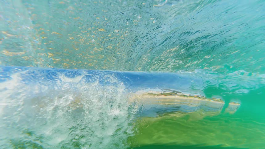 An underwater perspective reveals a vivid swirling wave as it breaks in shimmering blue and green tones