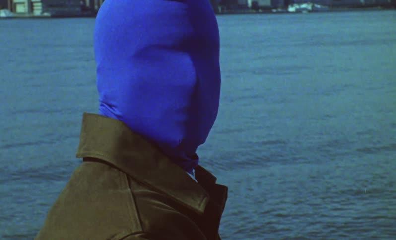 A model with a blue mask is standing in front of a waterfront city