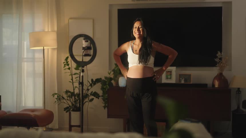 Pregnant woman in living room recording herself facing a smartphone on a tripod