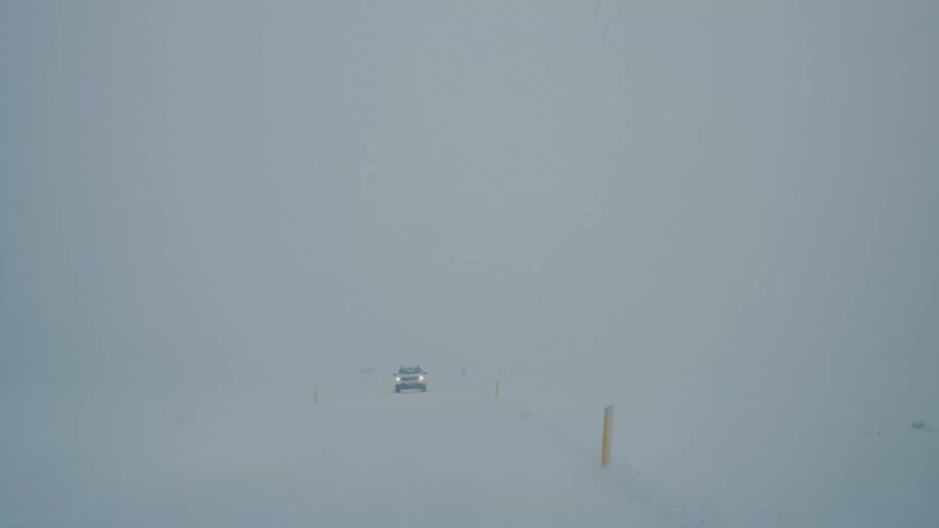 Car driving on a snowcovered road in heavy fog with reduced visibility and yellow posts marking the way