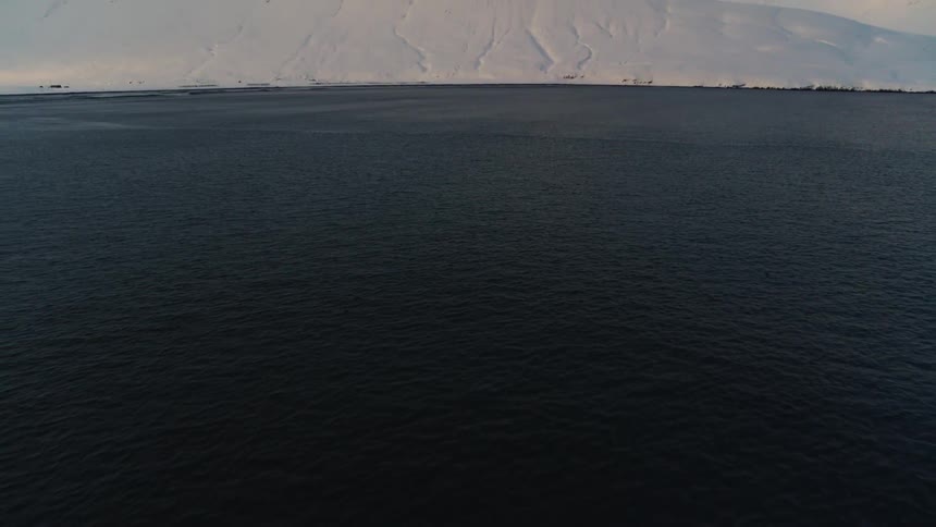 Aerial view of a calm sea surrounded by snowy mountains on a cloudy day
