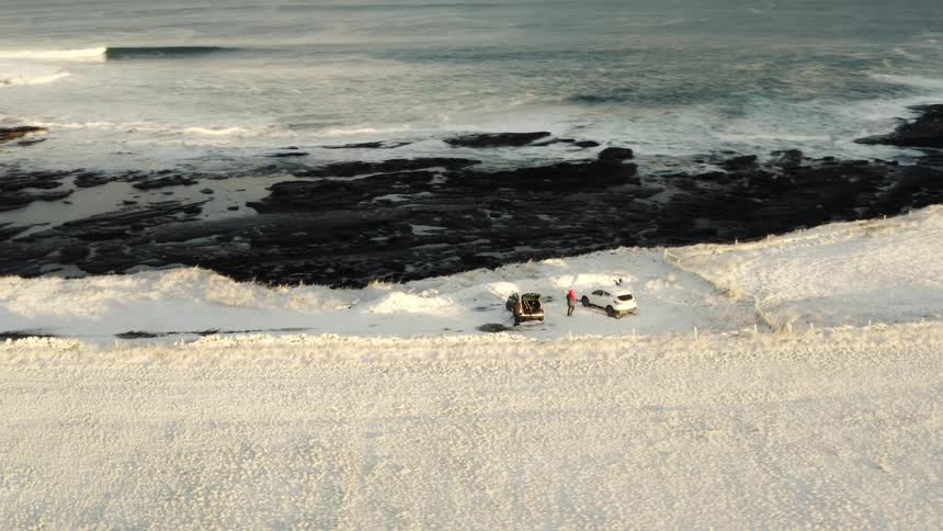 Aerial view of two vehicles parked in a snowy area facing a beach