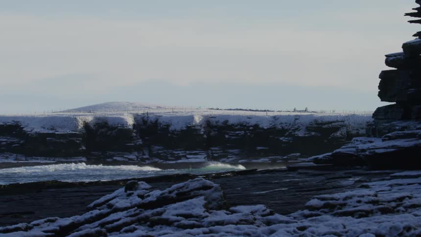 Small waves from the ocean crash on the shore that is covered in snow