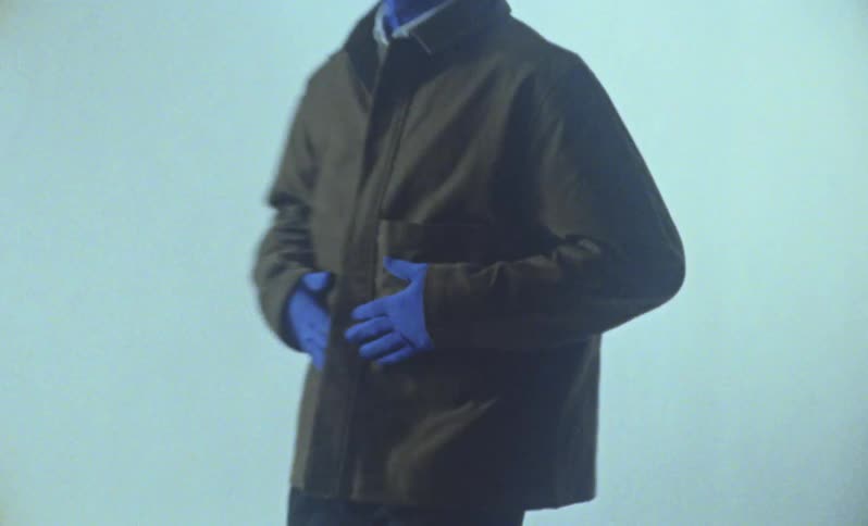 Blue man wearing brown jacket posing against white back drop for a photo shoot