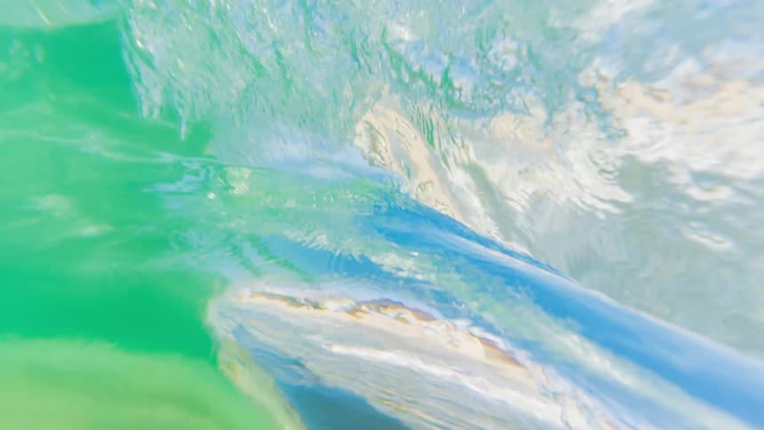 A dynamic inside view captures a cresting wave as it crashes close to the sandy shoreline