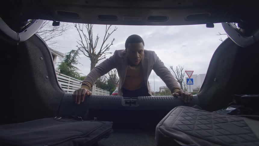A man puts a laptop bag inside a car trunk and takes out a roll of tape