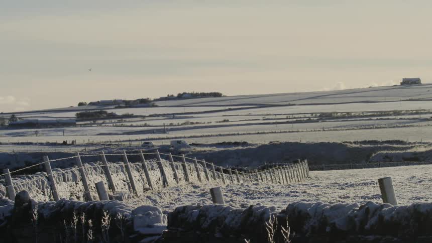 Vehicles park near fenced fields in the rural countryside on a snowy winter day